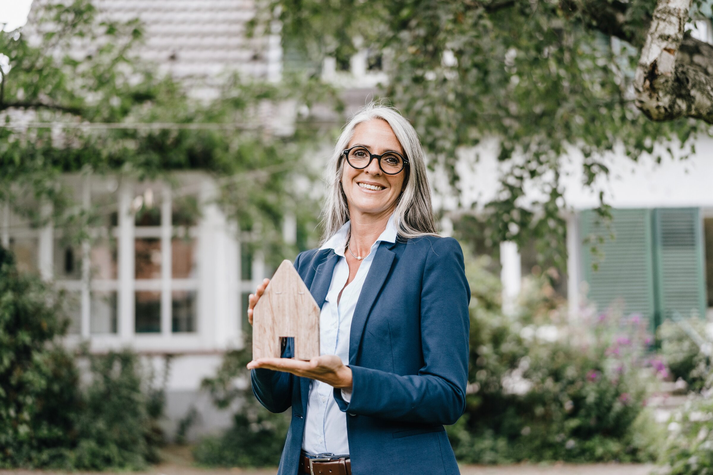 Weiterbildung im Bereich Immobilienverwaltung: Immobilienverwalterin hält Holzhausmodell.