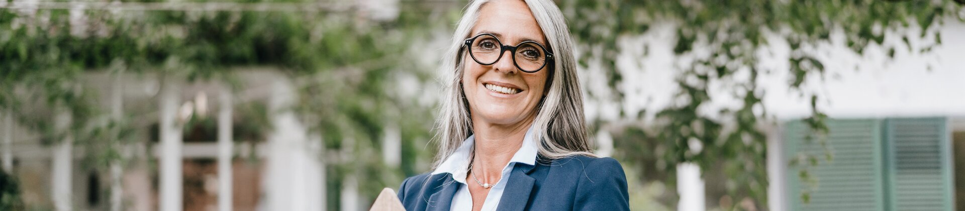 Maklerin hält symbolisches Holzhaus im Garten eines Wohnhauses