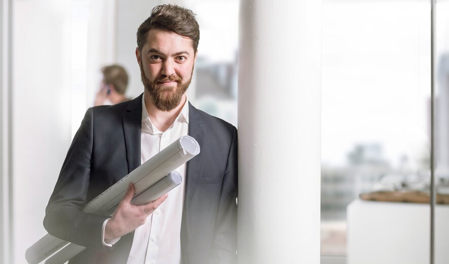 Architekt hält Baupläne im modernen Büro und lächelt in die Kamera