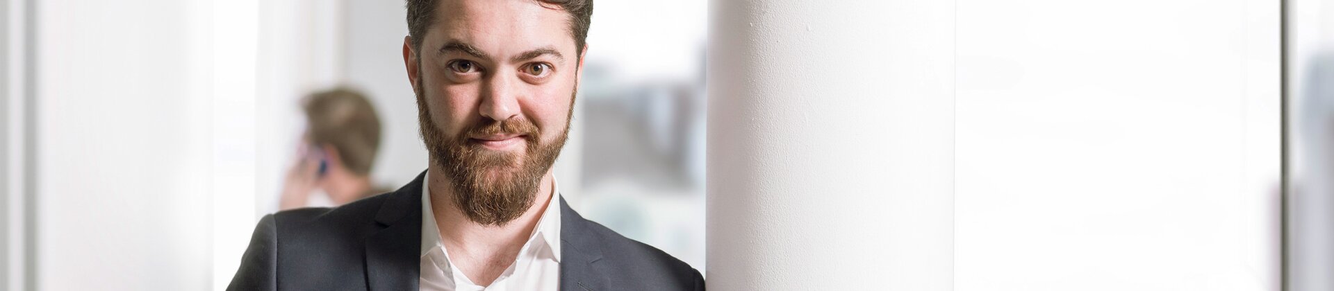 Architekt hält Baupläne im modernen Büro und lächelt in die Kamera