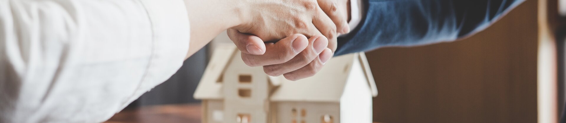 Handschlag beim Immobilienkauf mit Vertrag, Schlüssel und Hausmodell auf dem Tisch