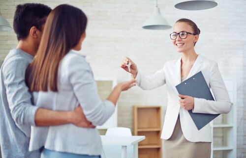 Weiterbildung für Immobilienmakler/-innen: Eine Immobilienmaklerin überreicht einem Paar die Schlüssel.