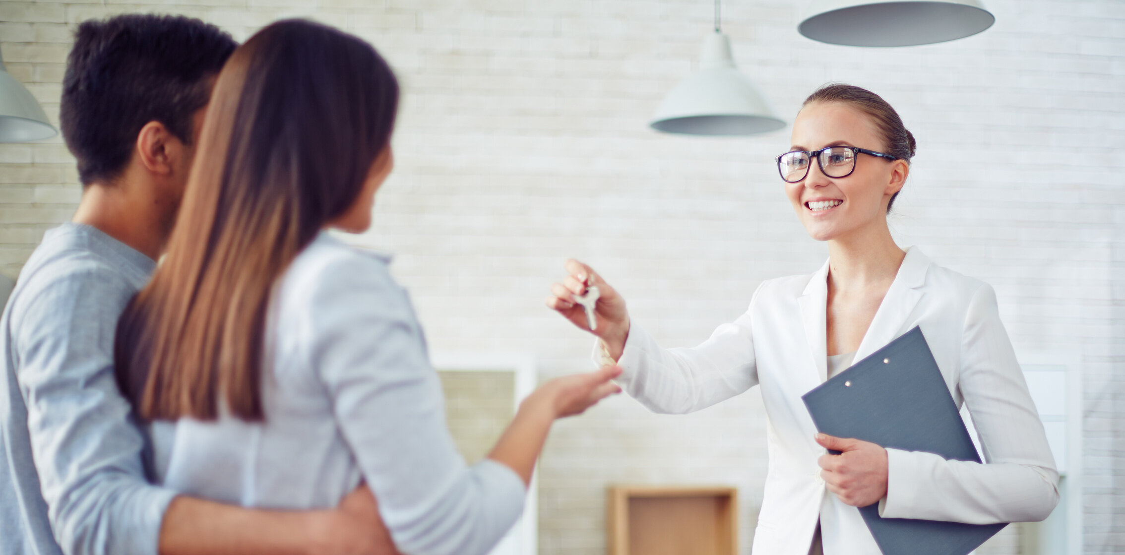 Weiterbildung für Immobilienmakler/-innen: Eine Maklerin überreicht einem jungen Paar die Schlüssel zu ihrem neuen Zuhause.