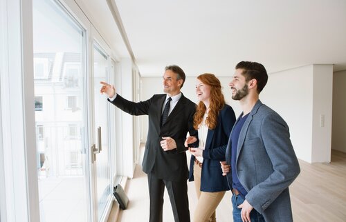 Weiterbildung für Immobilienmakler/-innen: Ein Immobilienmakler schaut sich mit einem Paar die Aussicht aus der Wohnung an