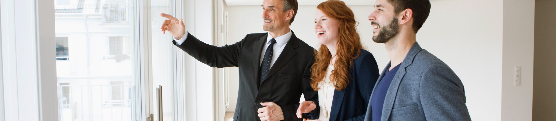 Makler zeigt einem Paar eine helle Immobilie bei einer Wohnungsbesichtigung