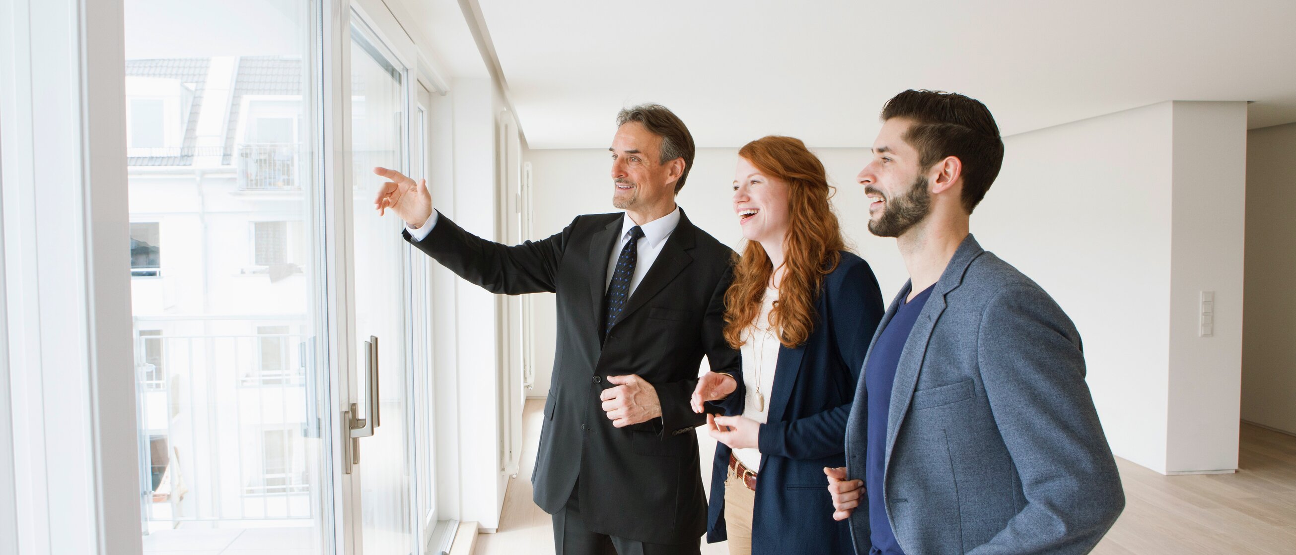 Weiterbildung für Immobilienmakler/-innen: Ein Immobilienmakler zeigt einem Paar die Aussicht aus der Wohnung