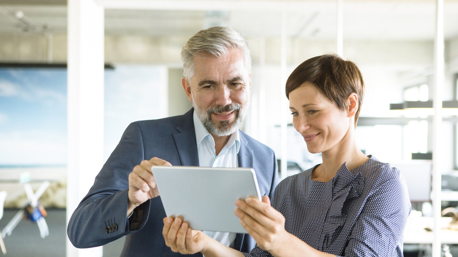 Zwei Geschäftsleute betrachten gemeinsam ein Tablet im modernen Büro