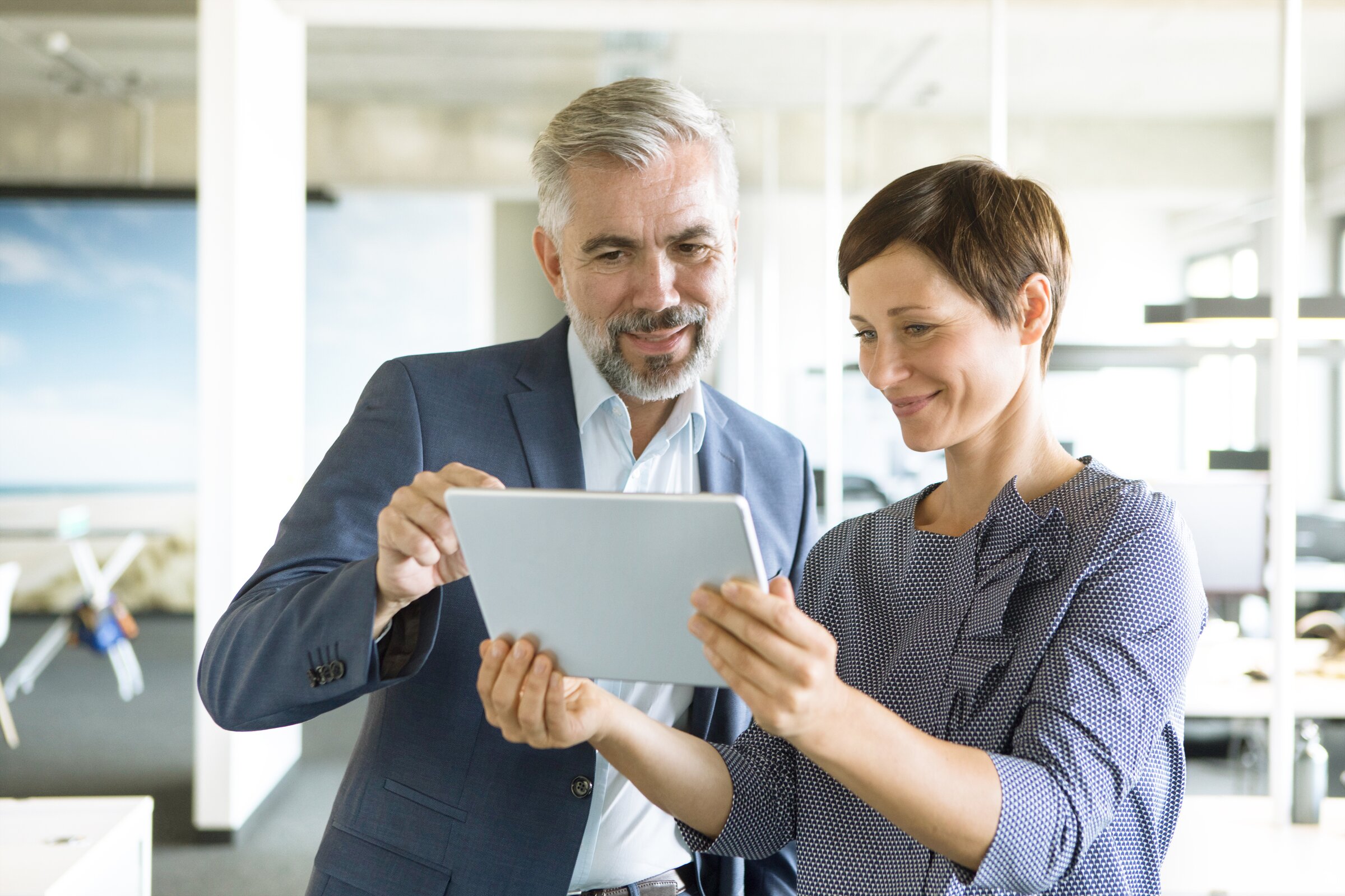 Zwei Geschäftsleute betrachten gemeinsam ein Tablet im modernen Büro