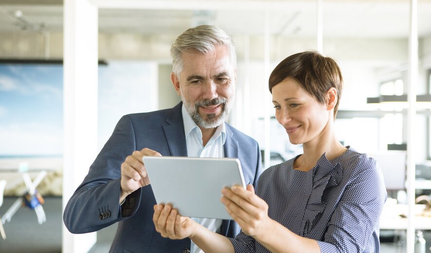 Zwei Geschäftsleute betrachten gemeinsam ein Tablet im modernen Büro