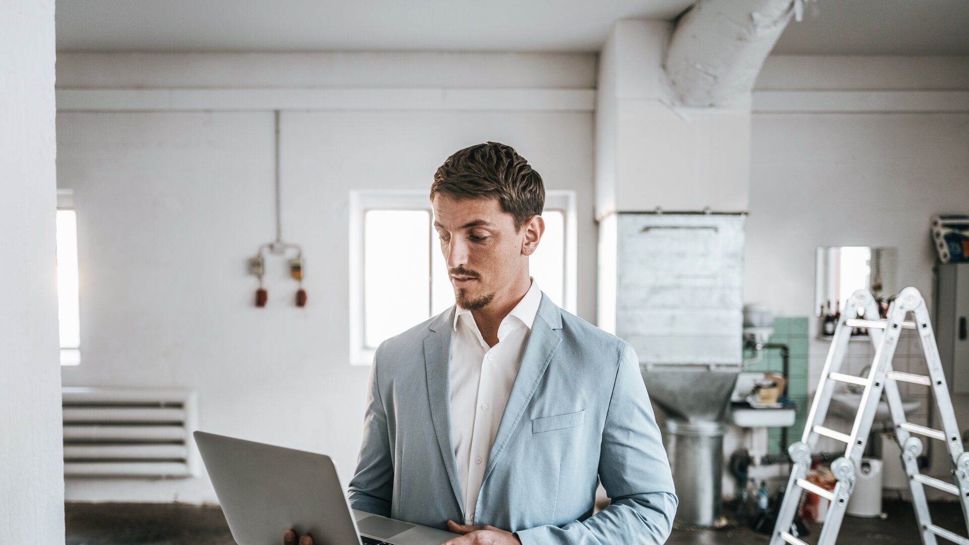 Immobilienverwalter inspiziert Objekt mit Laptop in renovierungsbedürftigem Raum