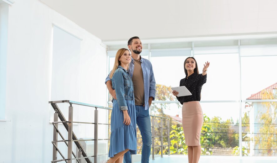 Maklerin zeigt jungem Paar eine helle Immobilie bei einer Wohnungsbesichtigung