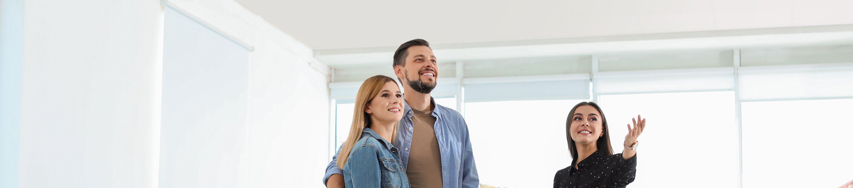 Maklerin zeigt jungem Paar eine helle Immobilie bei einer Wohnungsbesichtigung