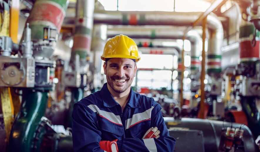 Industriearbeiter mit Schutzhelm lächelt in moderner Produktionsanlage