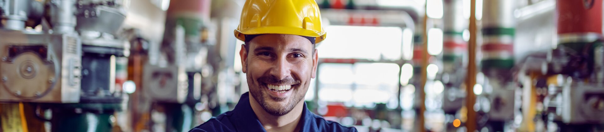Industriearbeiter mit Schutzhelm lächelt in moderner Produktionsanlage