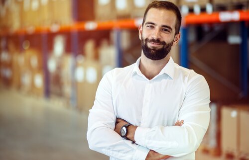 Lächelnder Logistikmitarbeiter im Lagerhaus mit verschränkten Armen