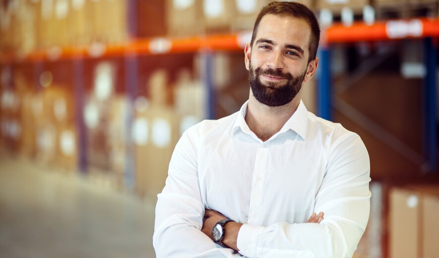 Lächelnder Logistikmitarbeiter im Lagerhaus mit verschränkten Armen