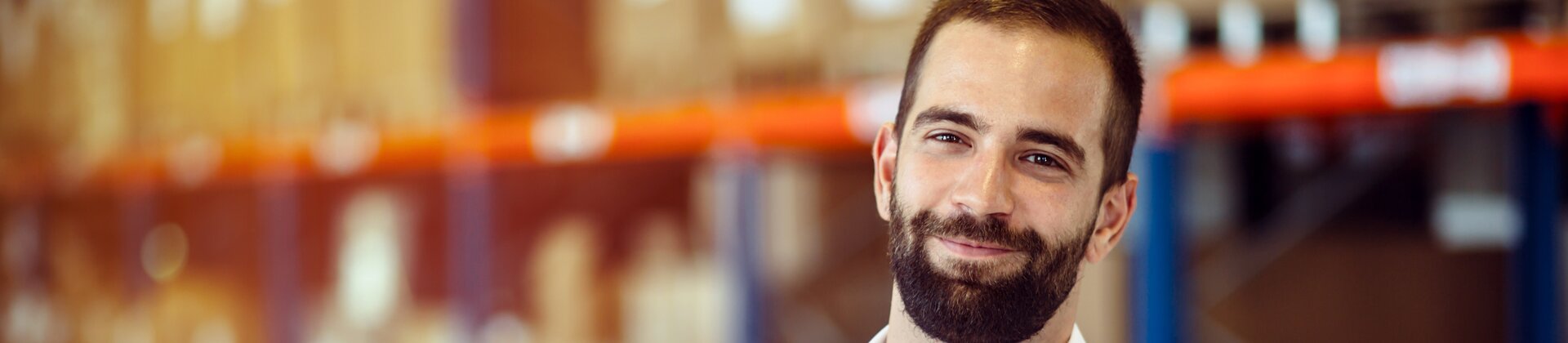 Lächelnder Logistikmitarbeiter im Lagerhaus mit verschränkten Armen