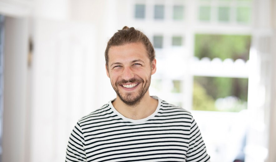 Lächelnder Mann in gestreiftem T-Shirt hält eine Tasse in heller, freundlicher Wohnumgebung