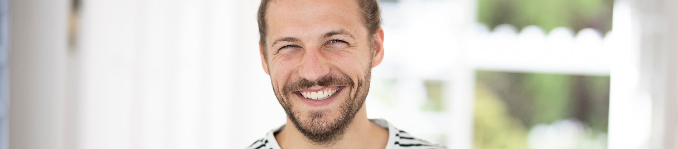 Lächelnder Mann in gestreiftem T-Shirt hält eine Tasse in heller, freundlicher Wohnumgebung