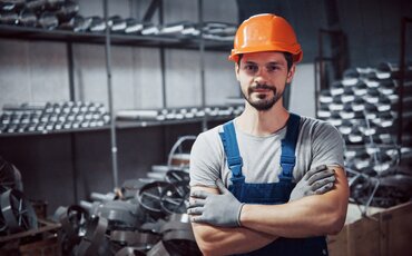 Industriemeister in Schutzhelm und Arbeitskleidung steht in einer Metallwerkstatt – Weiterbildung Gepr. Industriemeister/-in Metall bei der IHK Akademie München.