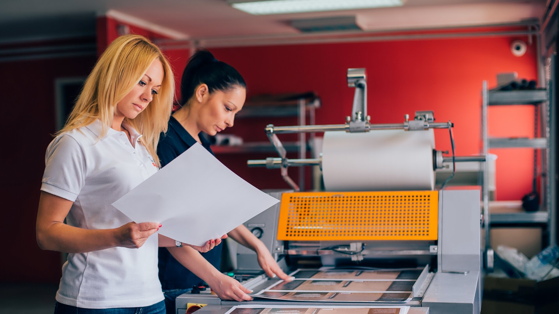 Druckereimitarbeiterinnen prüfen Druckbögen an moderner Produktionsmaschine