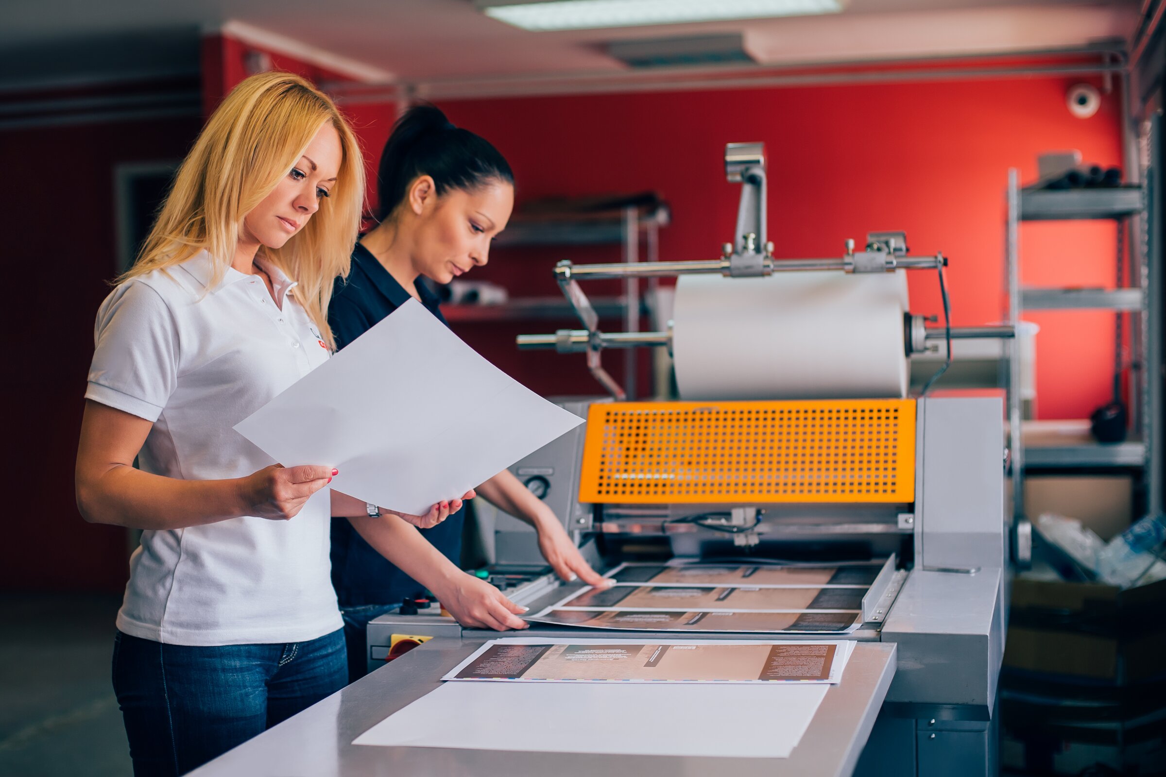 Druckereimitarbeiterinnen prüfen Druckbögen an moderner Produktionsmaschine