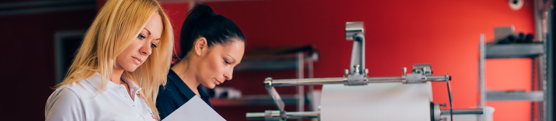 Druckereimitarbeiterinnen prüfen Druckbögen an moderner Produktionsmaschine