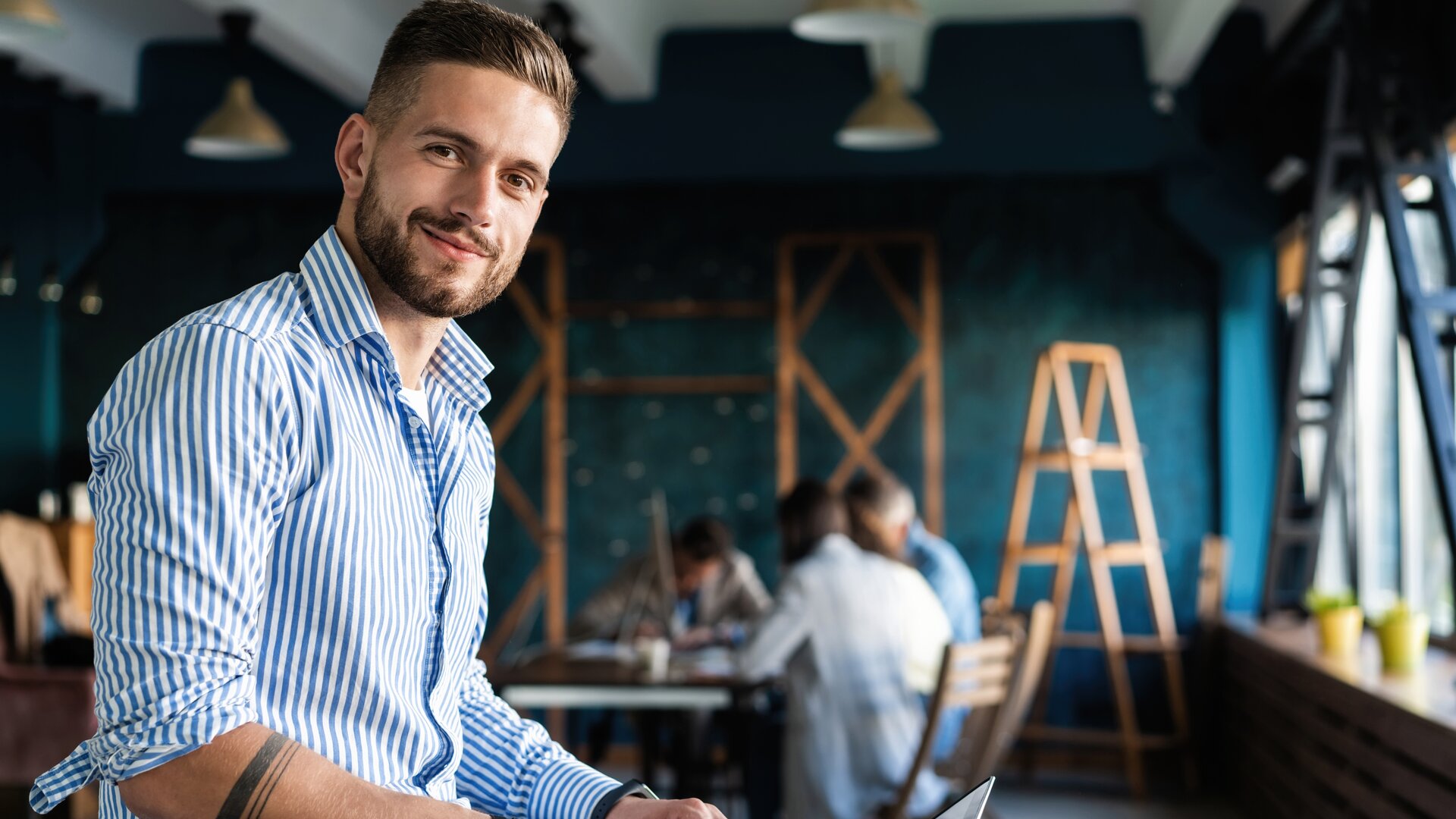 Junger Mann arbeitet lächelnd mit Laptop in modernem Coworking-Space