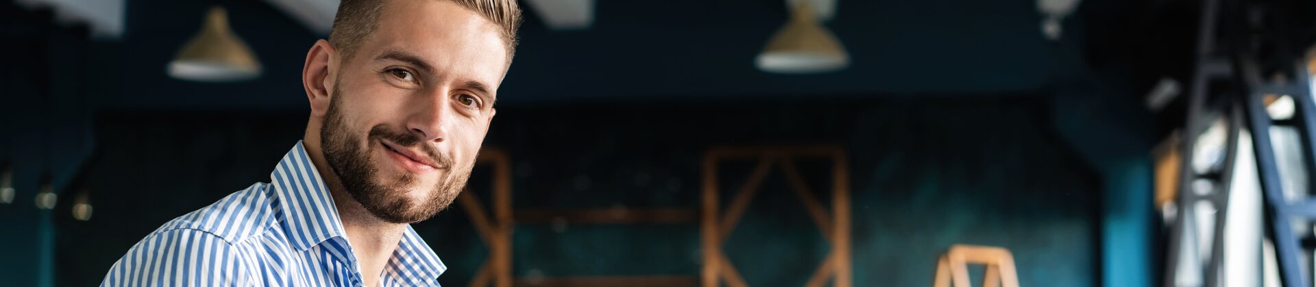 Junger Mann arbeitet lächelnd mit Laptop in modernem Coworking-Space