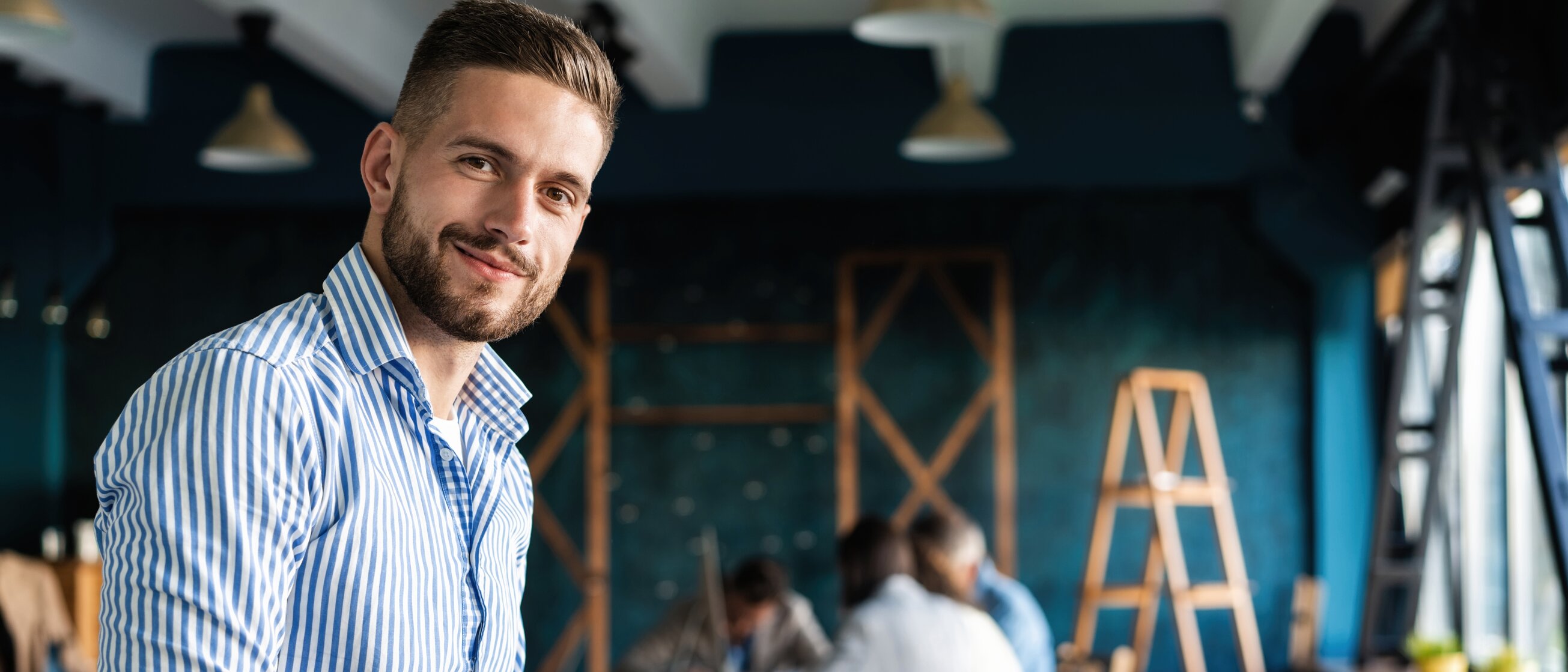 Junger Veranstaltungstechniker arbeitet lächelnd am Laptop in einem modernen Arbeitsraum – Sinnbild für Planung, Organisation und technische Leitung in der Weiterbildung zum Geprüften Meister für Veranstaltungstechnik.