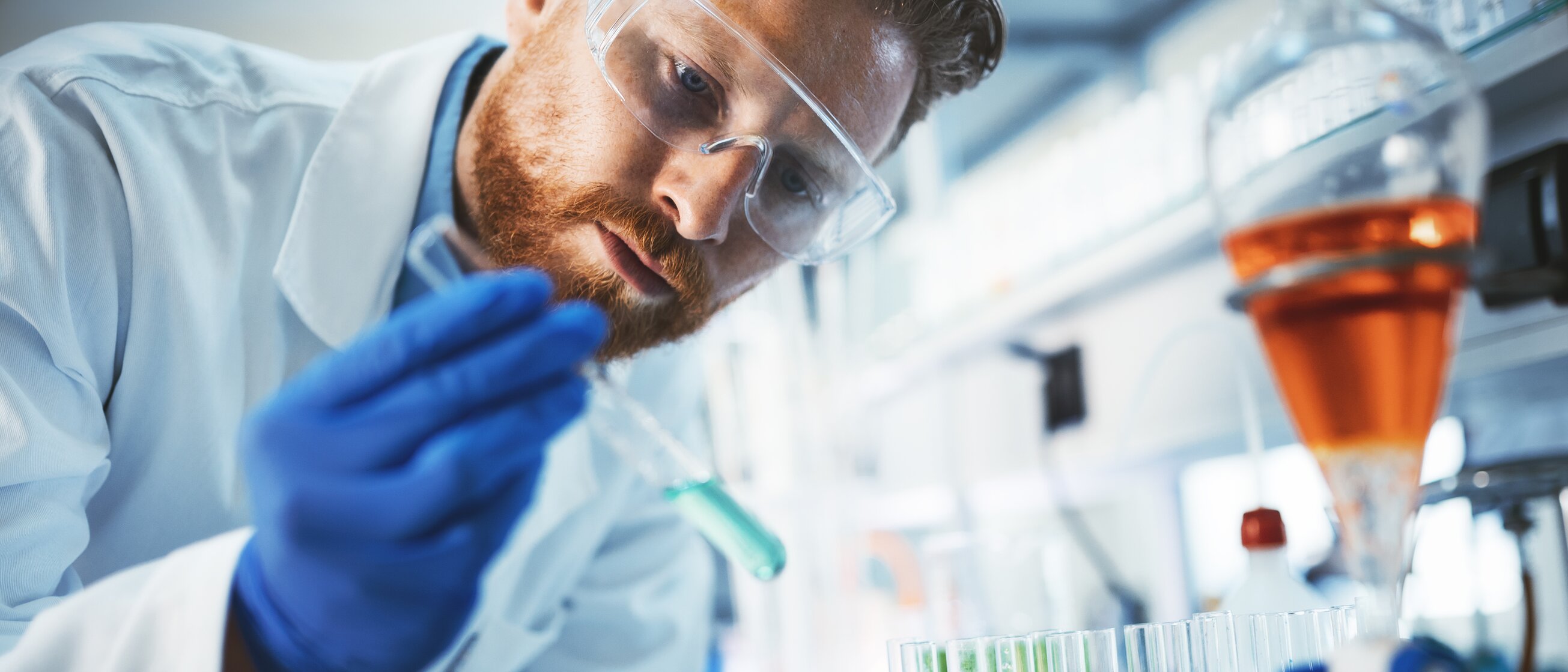 Chemielaborant im weißen Kittel arbeitet konzentriert mit Pipette und Reagenzgläsern im Labor – Symbol für die praktische Arbeit und Fachkompetenz in der Weiterbildung zum/zur Geprüften Industriemeister/-in Chemie.