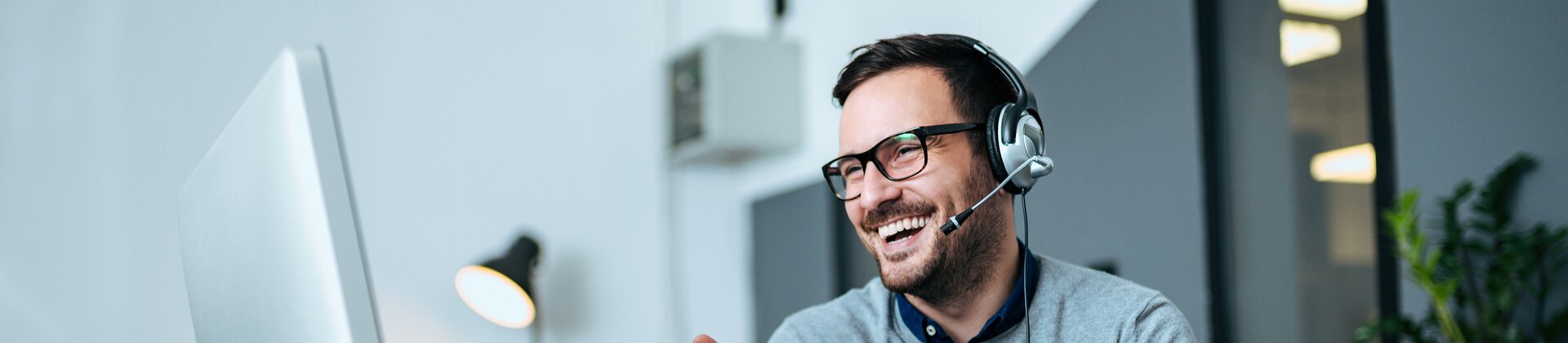 Mitarbeiter im Büro führt ein fröhliches Online-Meeting mit Headset am Computer durch.