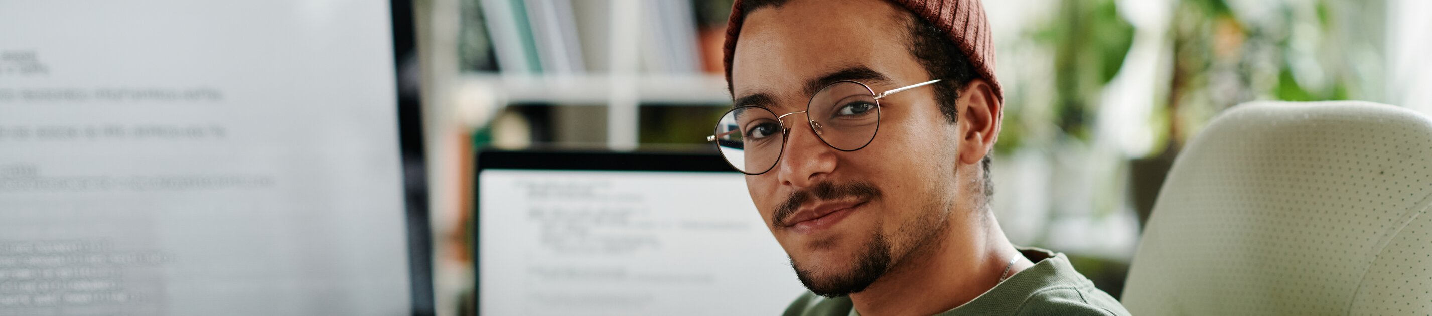 Junger Entwickler sitzt entspannt am Schreibtisch vor Monitoren mit Code und arbeitet an einem Softwareprojekt.