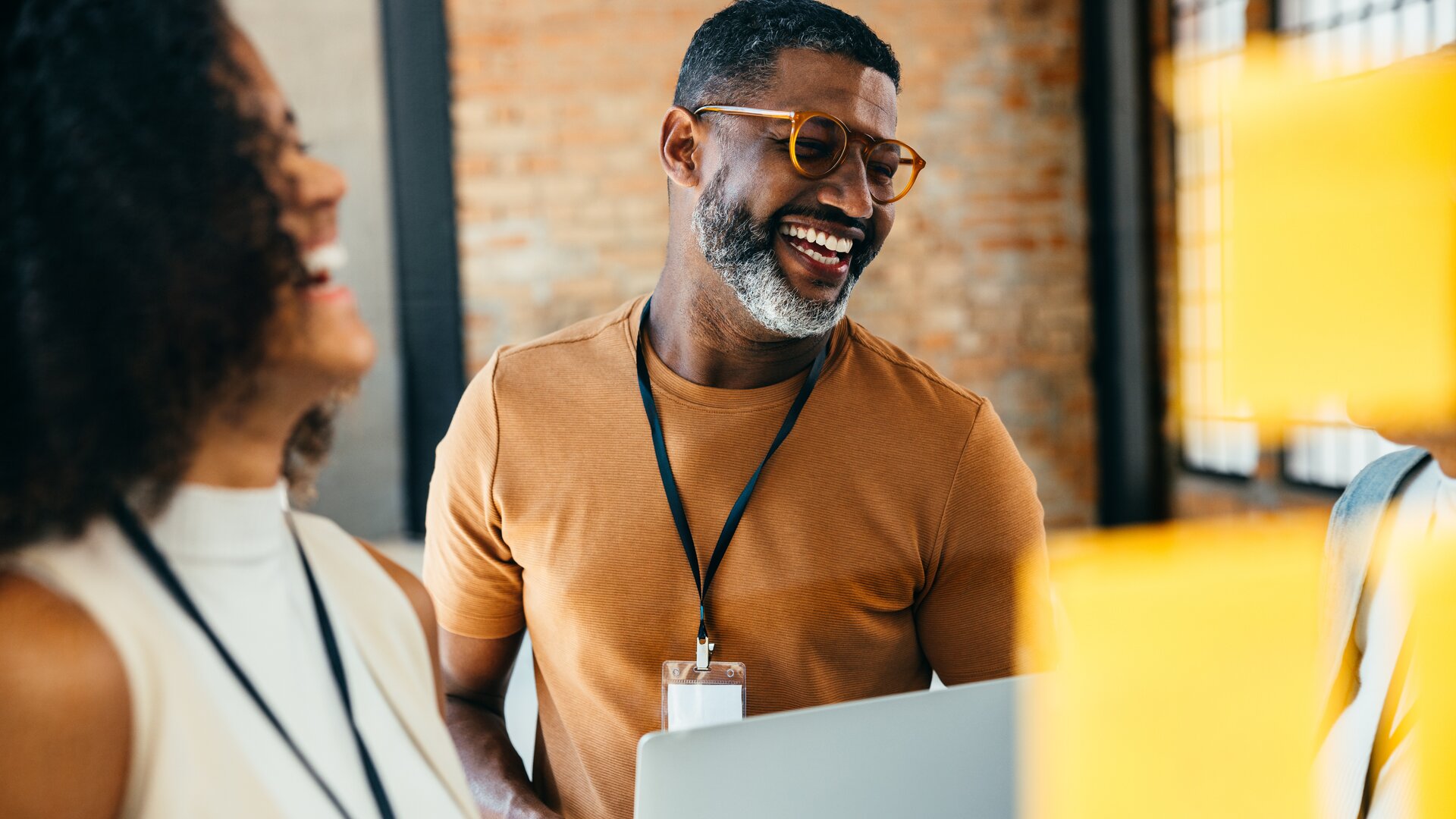 Teammeeting mit lächelndem Mitarbeiter, der einen Laptop hält und sich mit Kollegen austauscht.