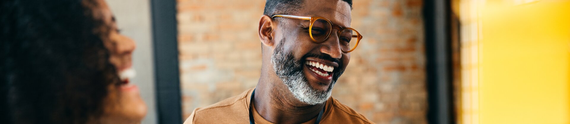 Teammeeting mit lächelndem Mitarbeiter, der einen Laptop hält und sich mit Kollegen austauscht.