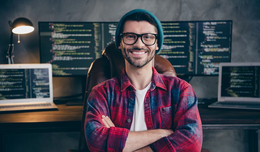 Programmierer sitzt vor mehreren Monitoren mit Code und arbeitet an Softwareentwicklung.