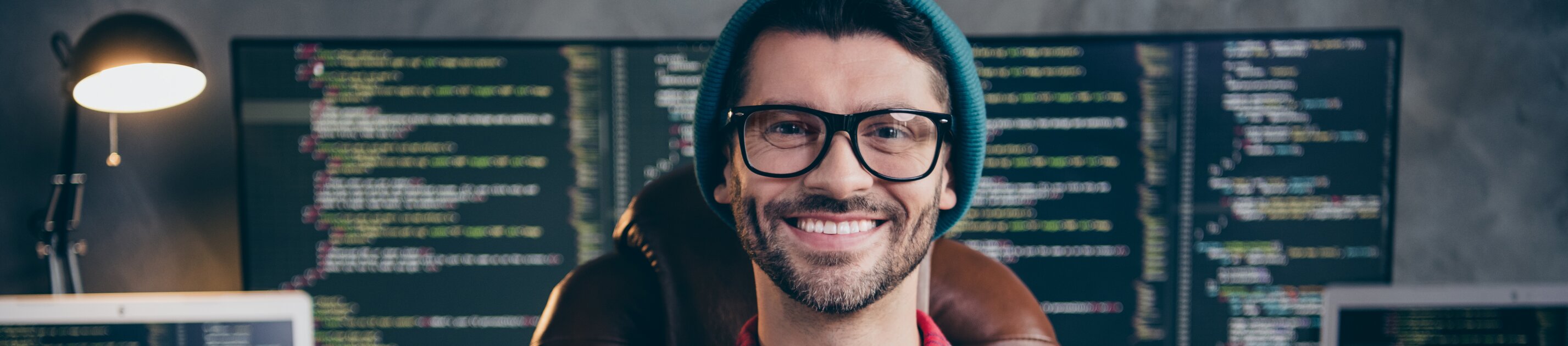 Programmierer sitzt vor mehreren Monitoren mit Code und arbeitet an Softwareentwicklung.