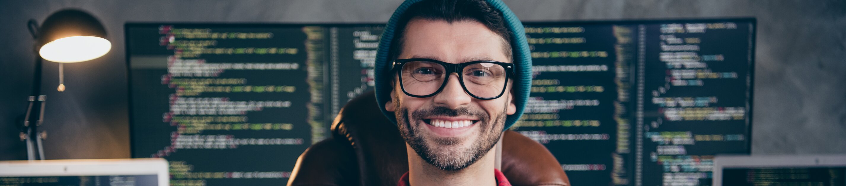 Programmierer sitzt vor mehreren Monitoren mit Code und arbeitet an Softwareentwicklung.