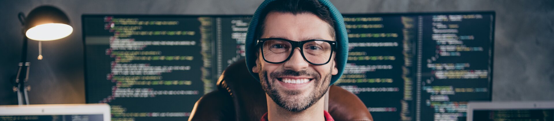 Programmierer sitzt vor mehreren Monitoren mit Code und arbeitet an Softwareentwicklung.