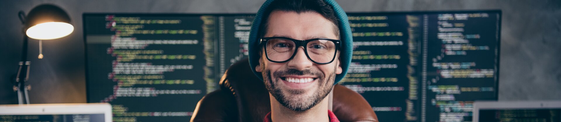 Programmierer sitzt vor mehreren Monitoren mit Code und arbeitet an Softwareentwicklung.