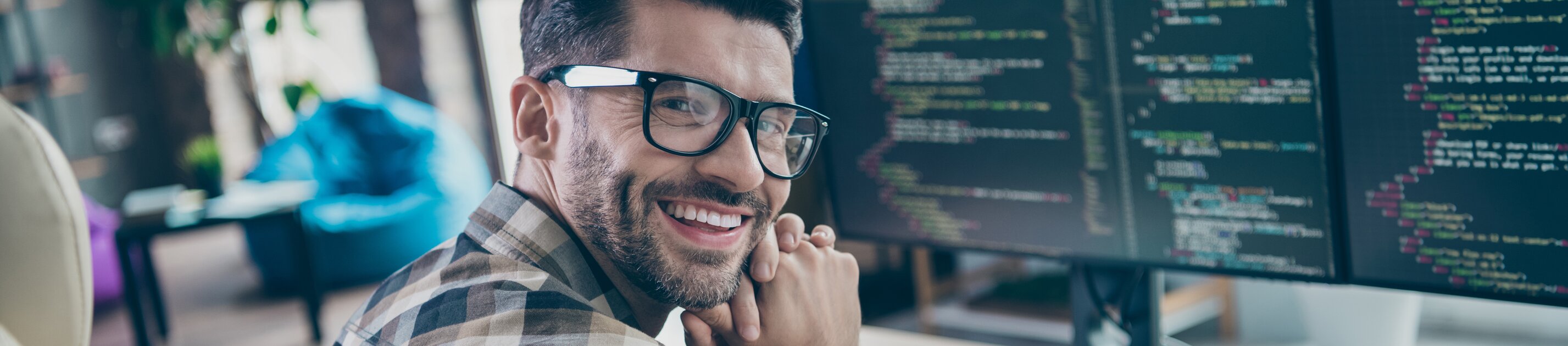 Lächelnder Programmierer arbeitet am Computer mit Code auf mehreren Monitoren.