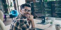 Lächelnder Programmierer arbeitet am Computer mit Code auf mehreren Monitoren.