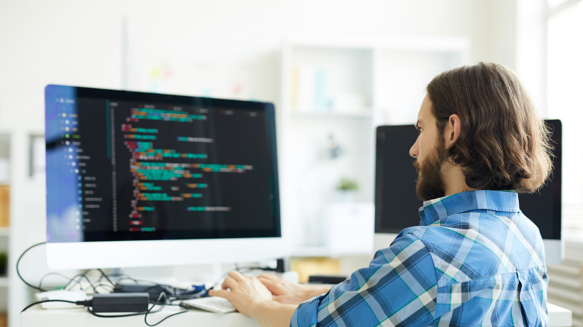 Softwareentwickler programmiert an großem Monitor in modernem Büro.