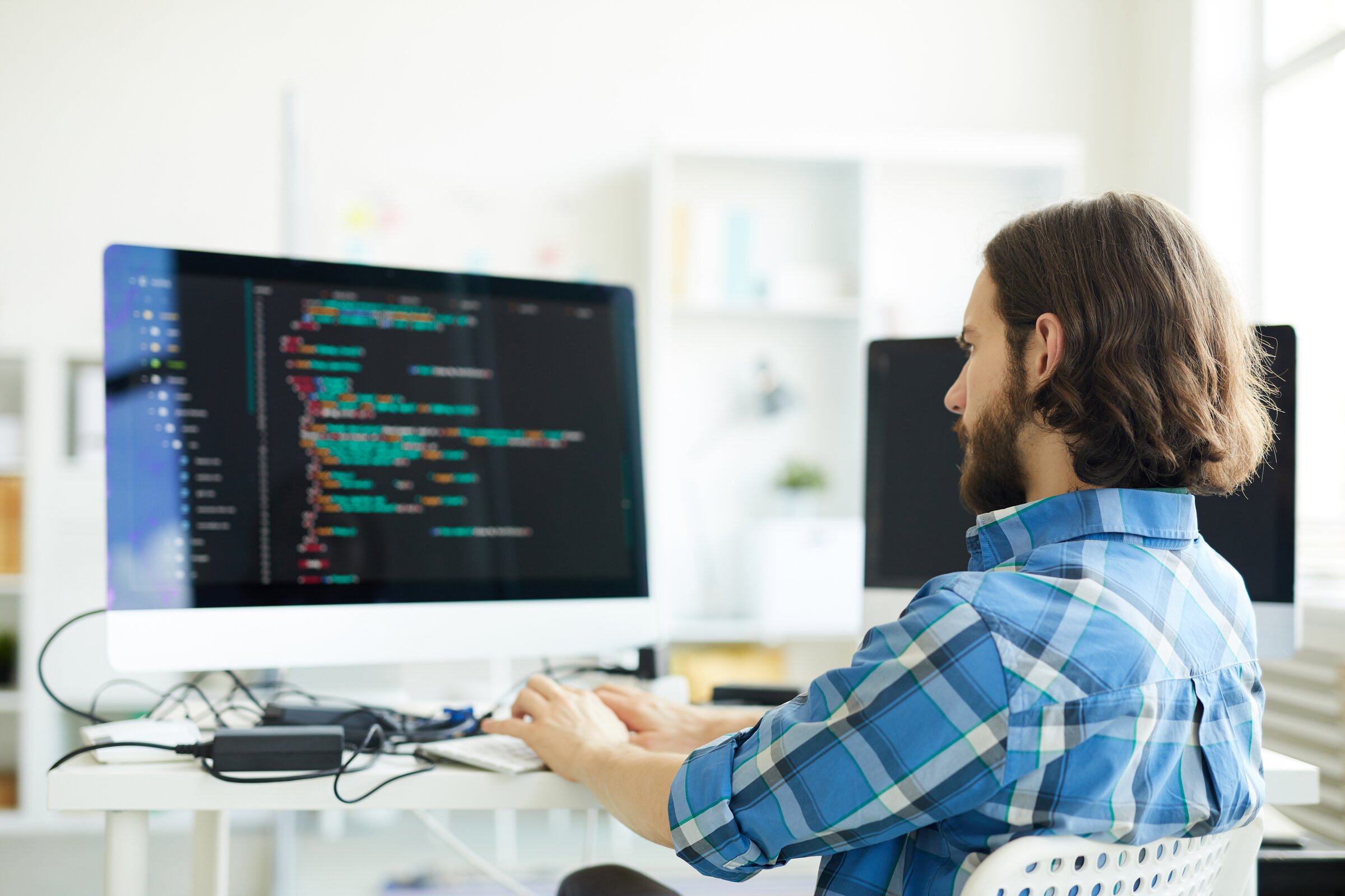 Ein IT-Fachmann arbeitet konzentriert am Computer, auf dessen Bildschirm Programmcode zu sehen ist – Symbol für Datensicherheit, Informationsschutz und technische Datenschutzprozesse.