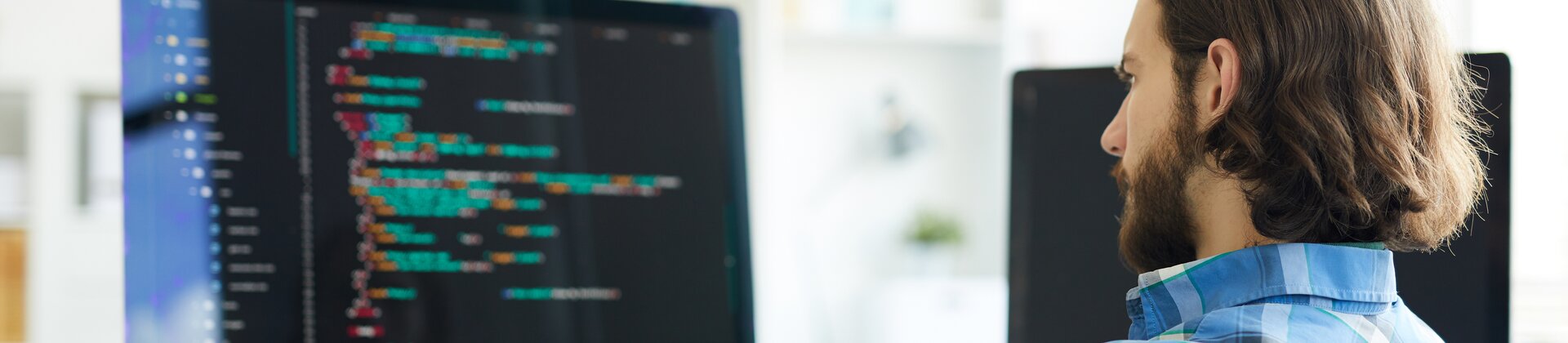 Softwareentwickler programmiert an großem Monitor in modernem Büro.