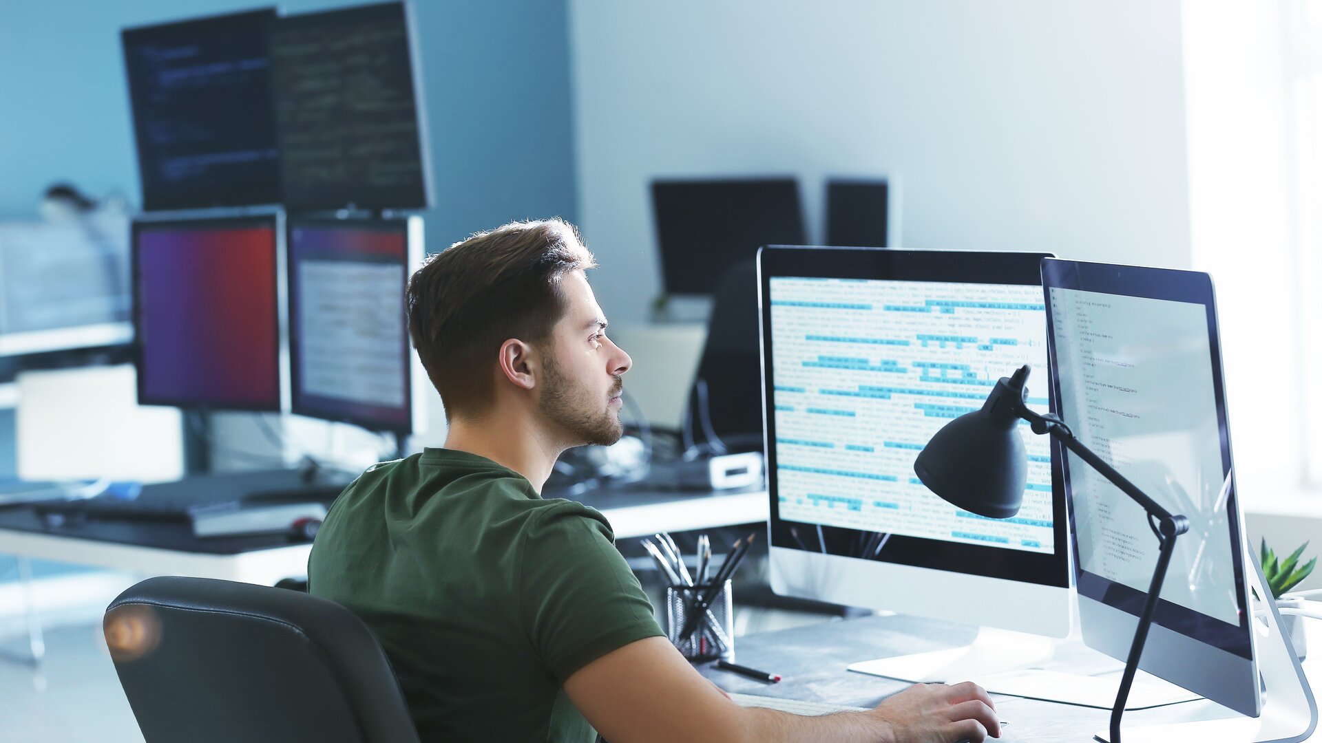 Programmierer arbeitet konzentriert am Computer mit mehreren Monitoren im modernen Büro.