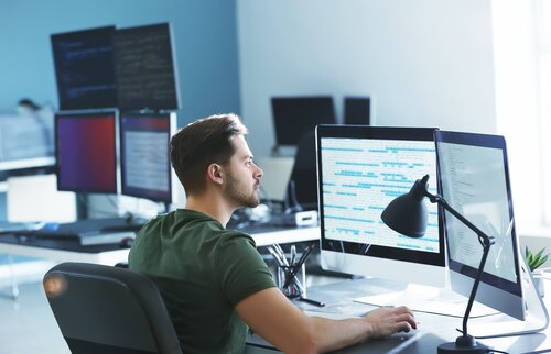 oftwareentwickler überwacht Code und Systeme an mehreren Bildschirmen.