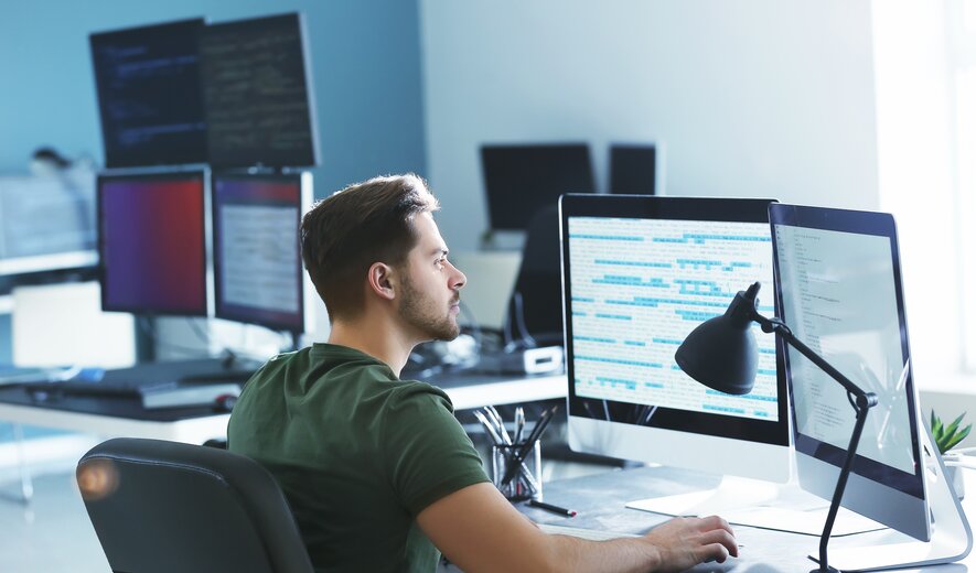 Programmierer arbeitet konzentriert am Computer mit mehreren Monitoren im modernen Büro.