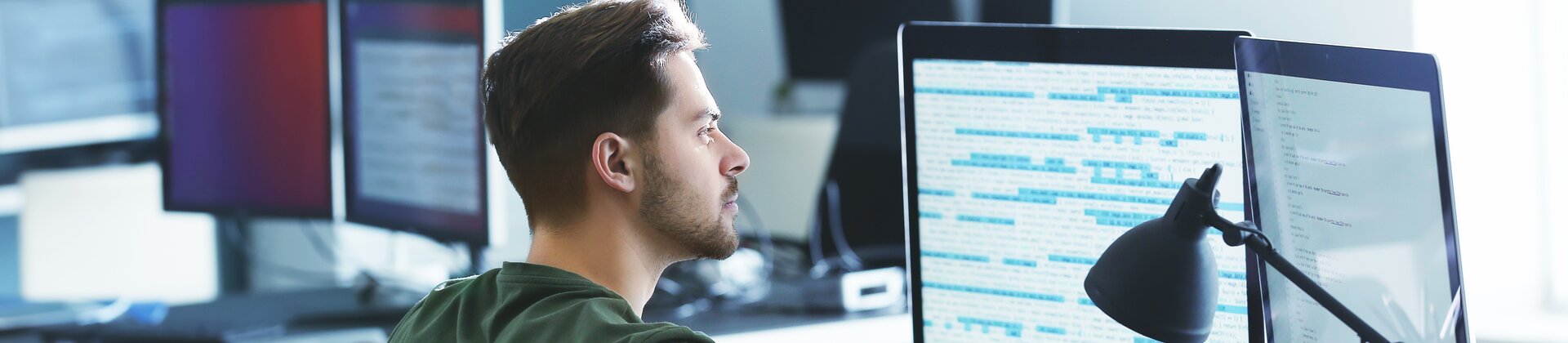 Programmierer arbeitet konzentriert am Computer mit mehreren Monitoren im modernen Büro.