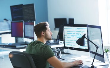 Programmierer arbeitet konzentriert am Computer mit mehreren Monitoren im modernen Büro.